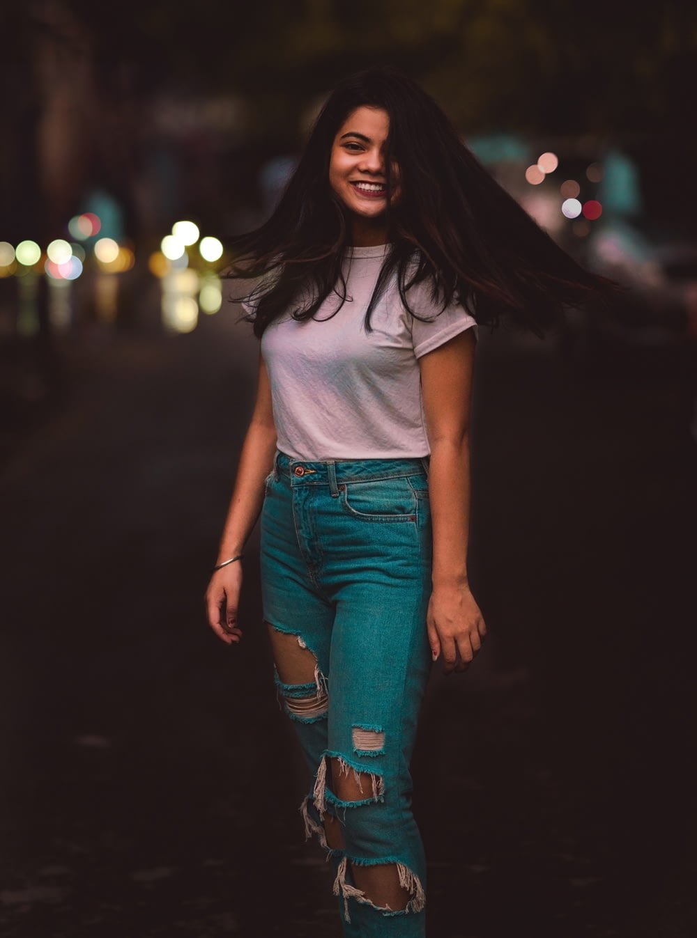 woman in white crew-neck T-shirt and distressed teal jeans waving hair
