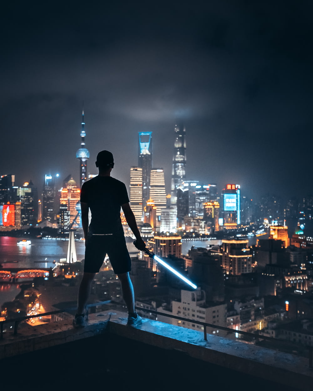 man holding lightsaber while standing on ledge overlooking city