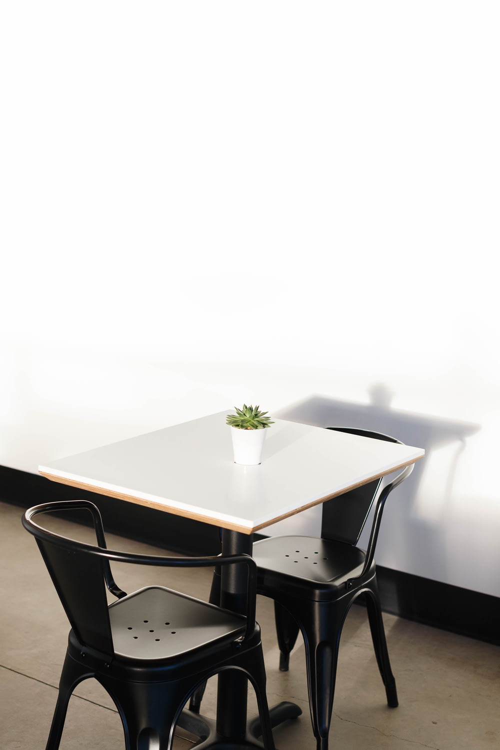 mesa quadrada de madeira branca com duas cadeiras pretas