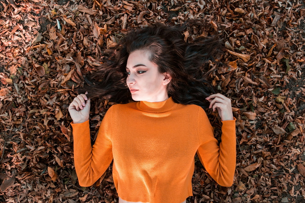 woman wearing orange long-sleeved shirt lying on brown ground with leaves