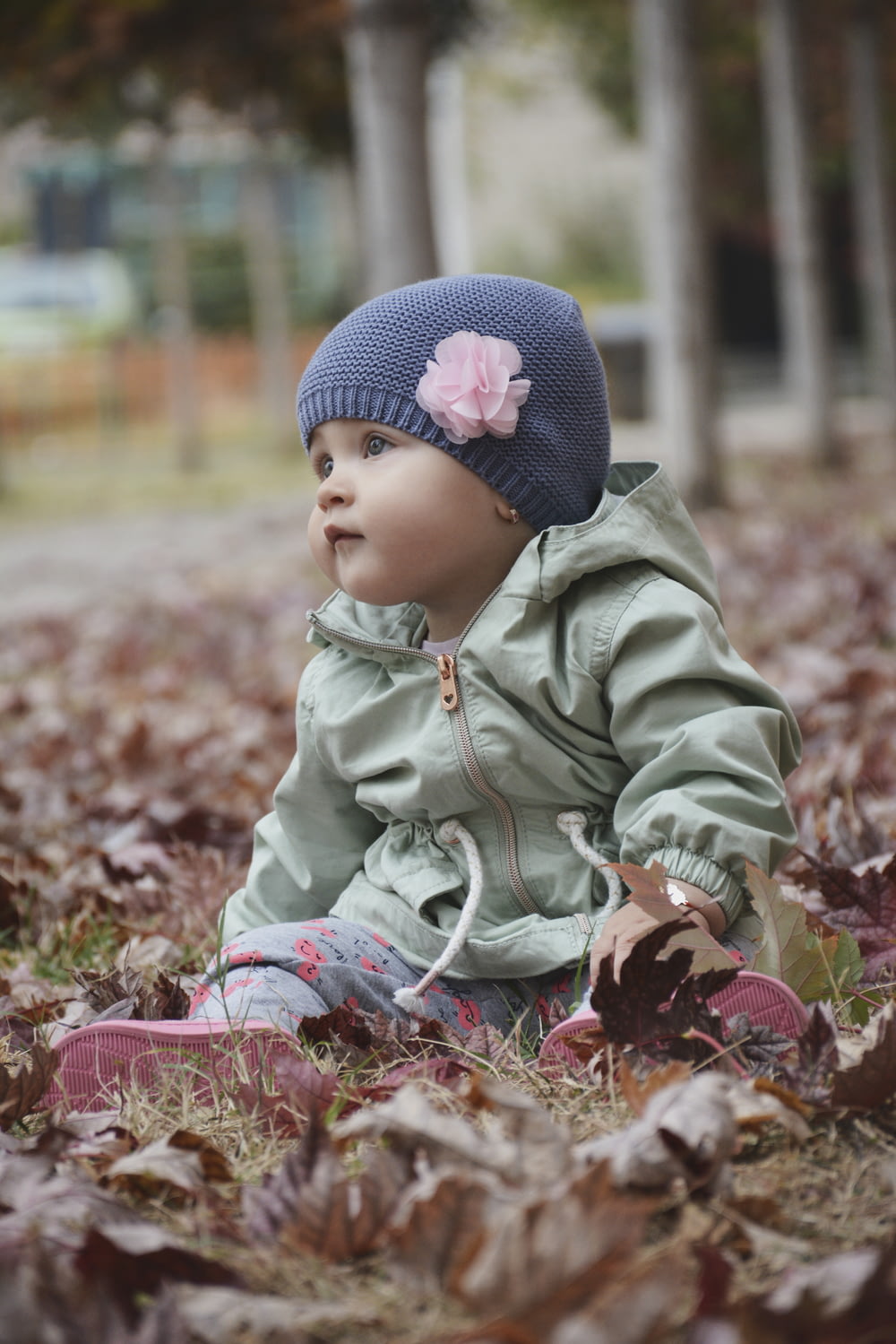 baby wearing gray beanie cap sitting surrounded by dried leaves