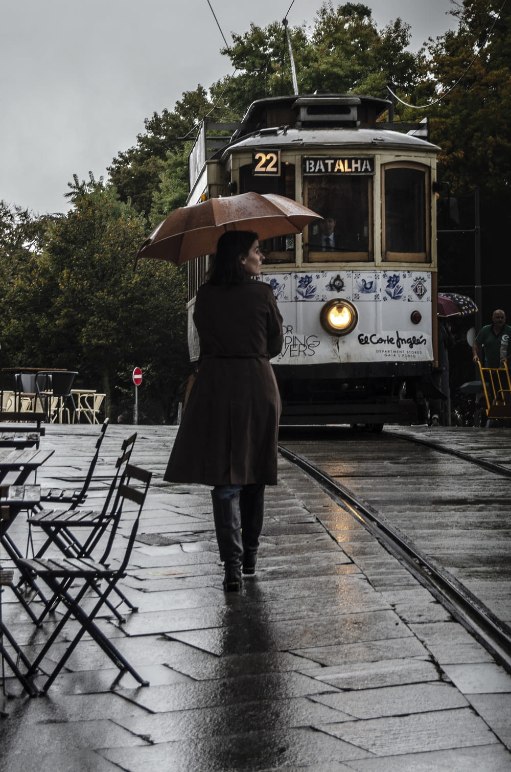 woman wearing brown coat walking on street while holding umbrella