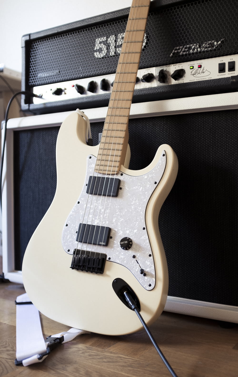 white and black electric guitar beside black guitar amplifier