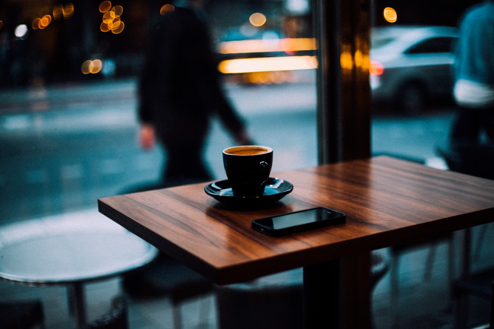xícara de café e smartphone em cima da mesa de jantar de madeira
