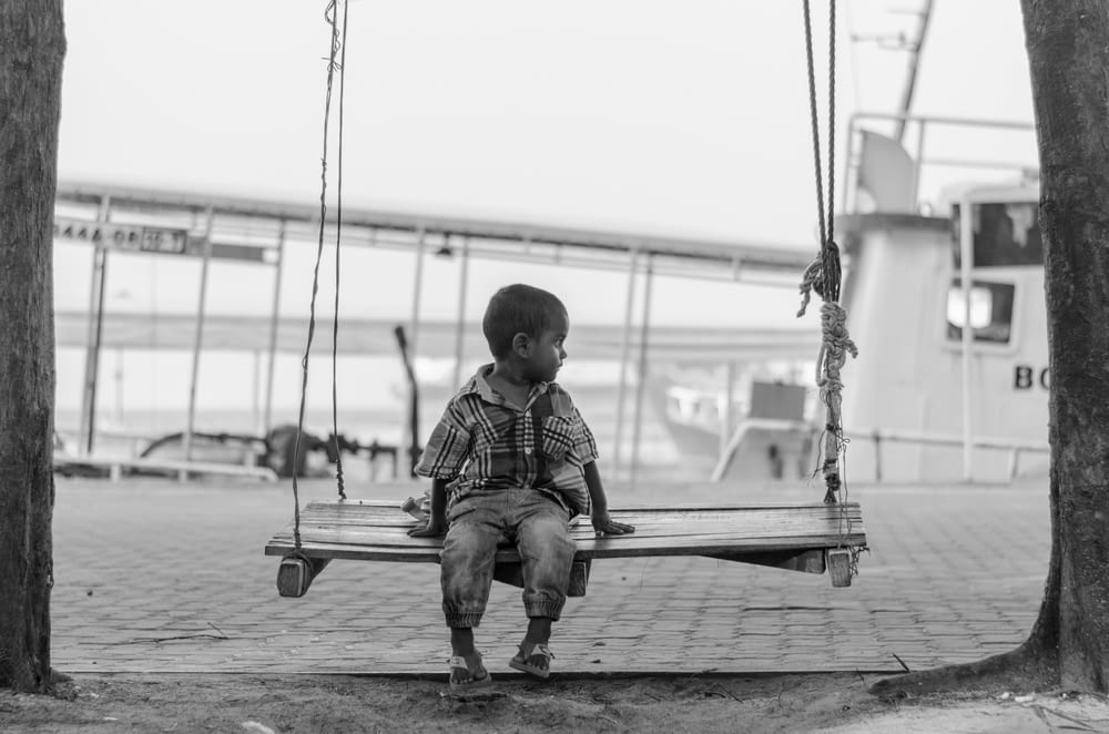grayscale photo of boy sitting of swing chair