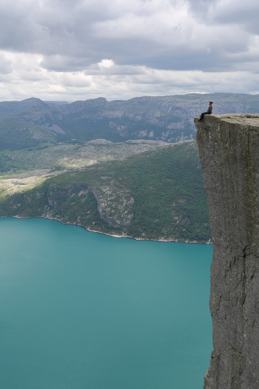 person sits on cliff over the lake