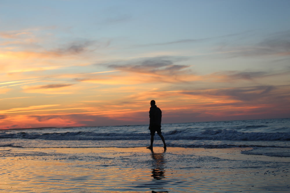 silhouette of man walking on seashore