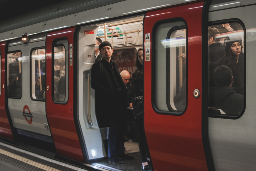 a man standing on a train platform next to a red and silver train