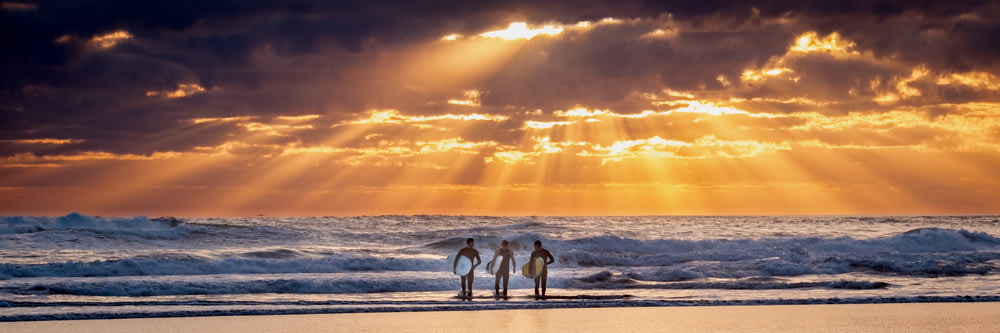 trois hommes tenant une planche de surf face aux vagues de la mer