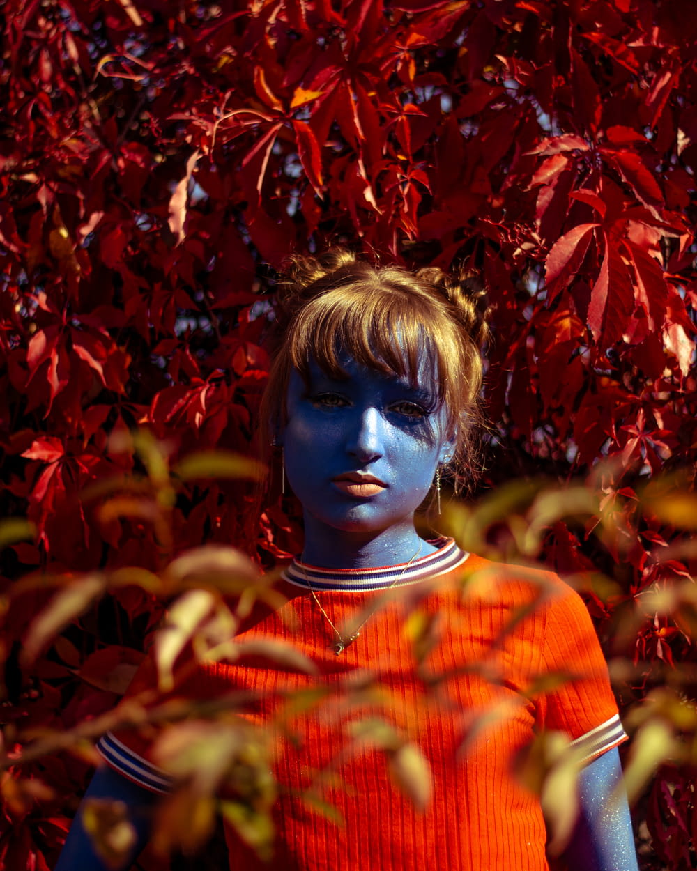 Menina de pele azul vestindo camisa vermelha de gola de tripulação cercada por folhas de bordo vermelhas