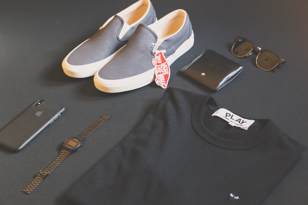 Camisa de juego negra doblada junto al iPhone X, reloj digital y zapatillas