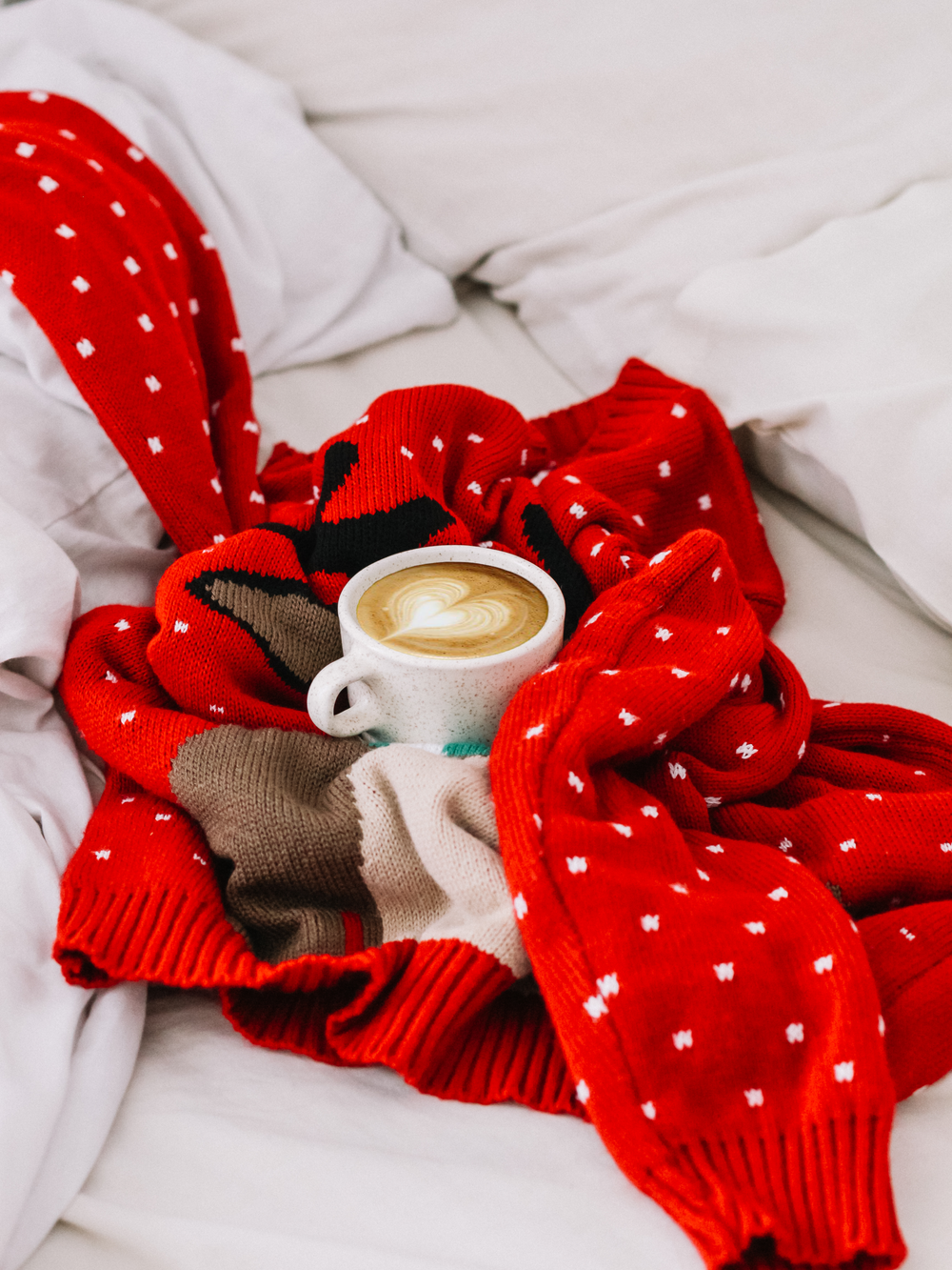 Caneca redonda de cerâmica branca com bebida de café dentro em cima de suéter de malha de bolinhas vermelhas e brancas
