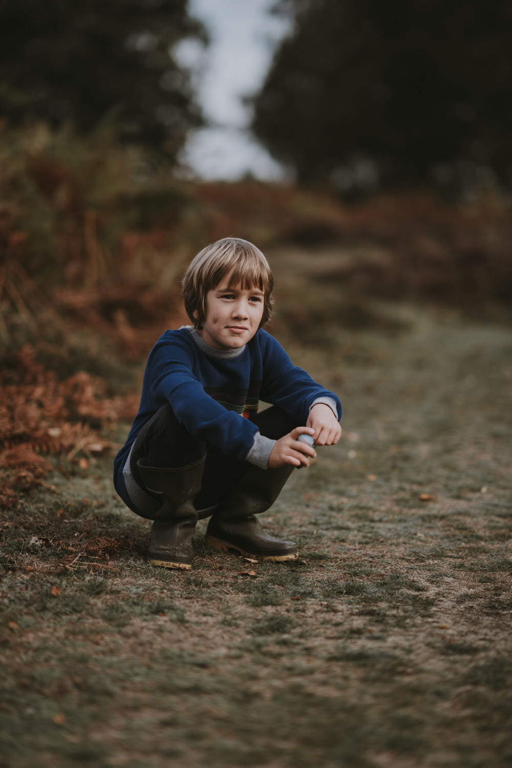boy in blue sweater squatting down on brown pathway