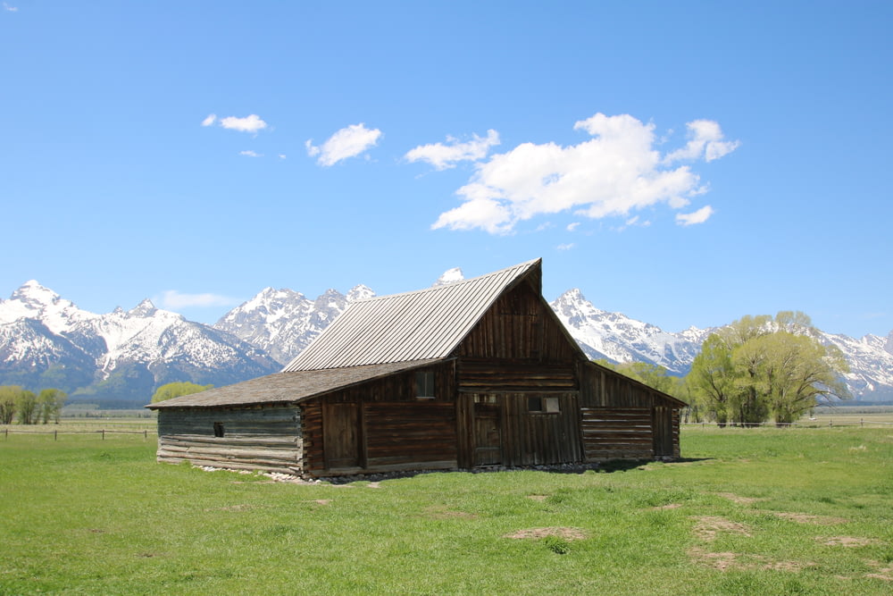 brown wooden barn near snow-covered mountain during day time