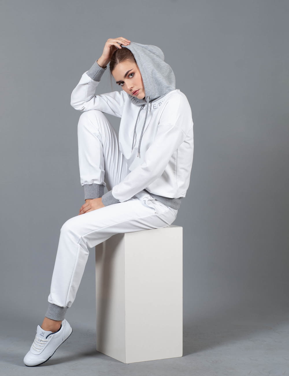 woman sitting on white box wearing hoodie holding her head