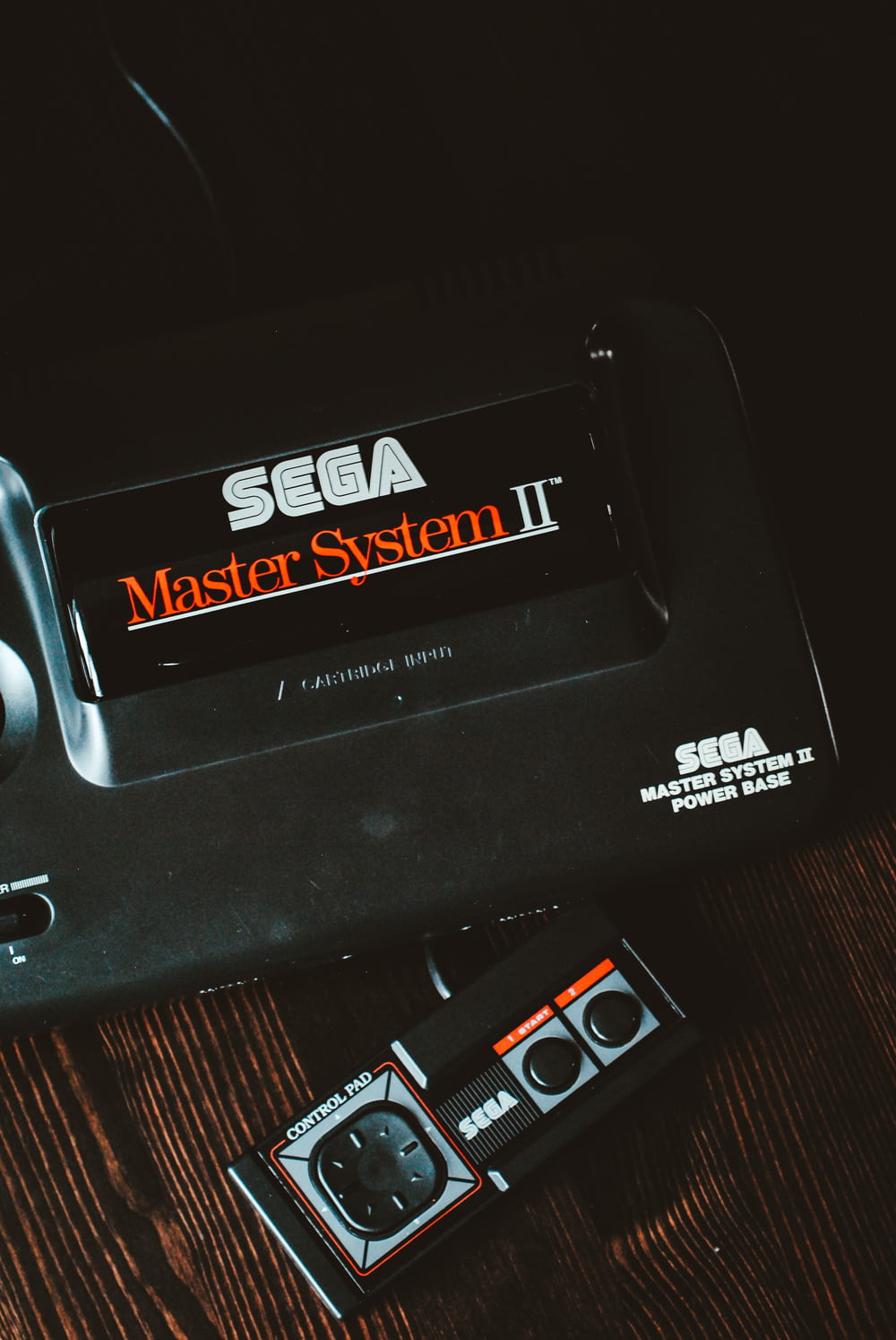 black Sega Master System II device on brown wooden surface