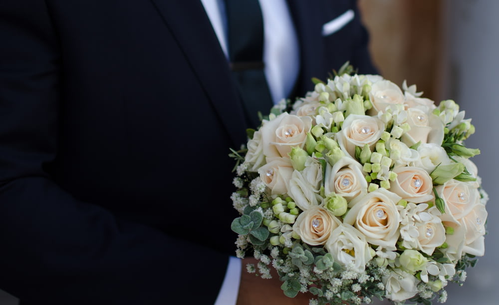 homme portant un costume noir tenant un bouquet de roses blanches