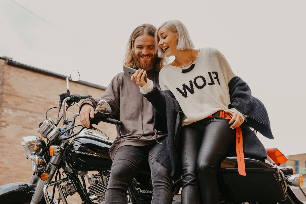 woman and man sitting on motorcycle while holding phone