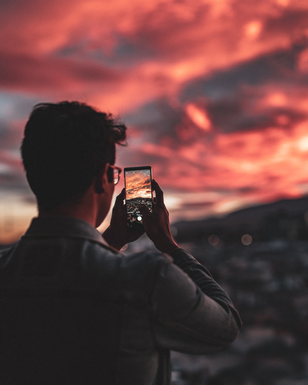 man taking phone picture of red sky