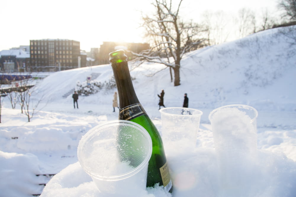 wine bottle beside disposable cups on snow