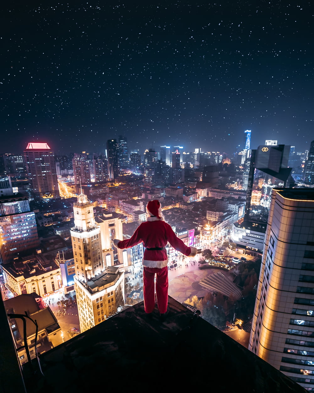 persona che indossa il vestito di Babbo Natale in piedi sul bordo dell'edificio di notte