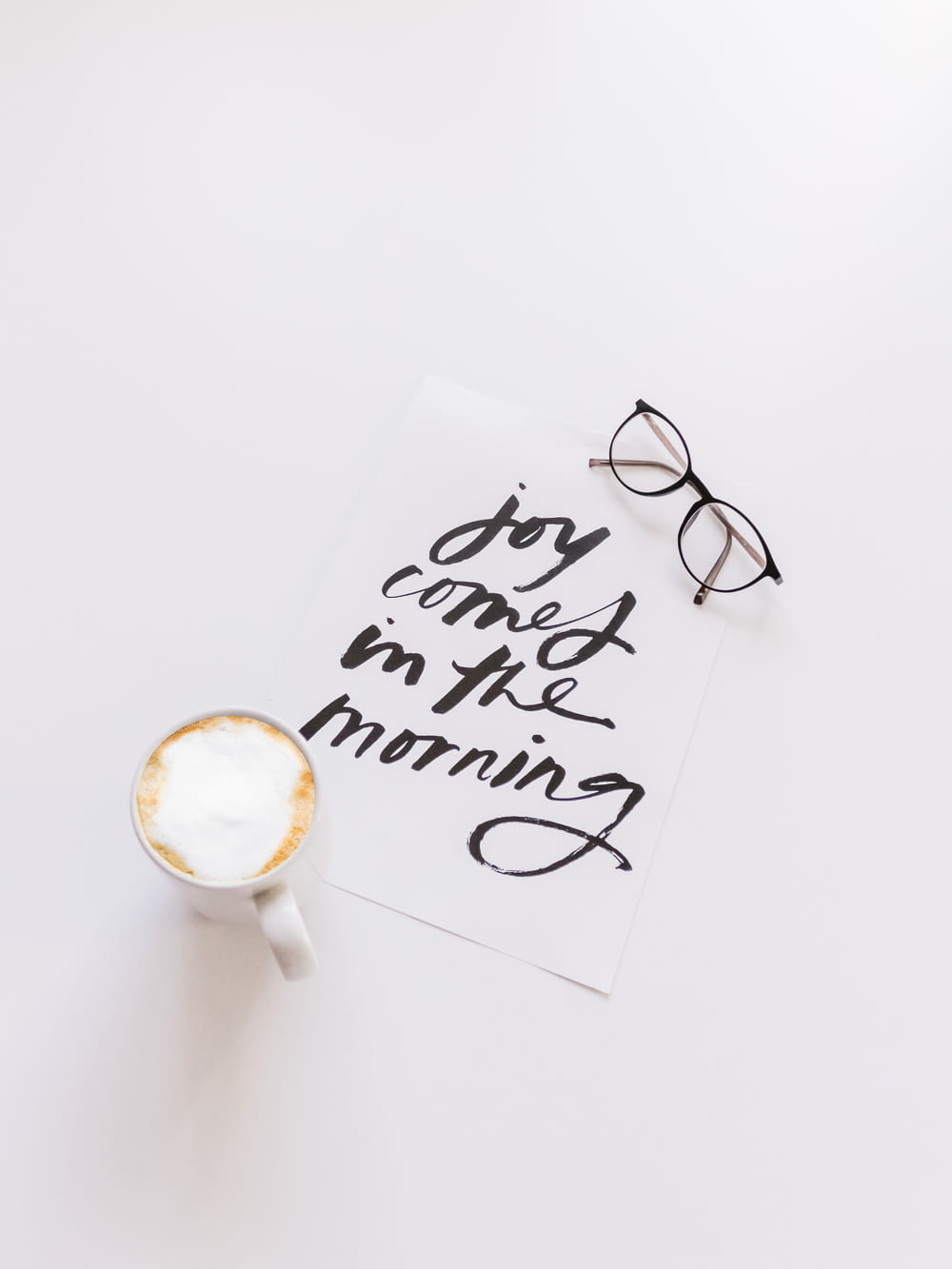 occhiali da vista con montatura nera accanto a una tazza di caffè in ceramica bianca