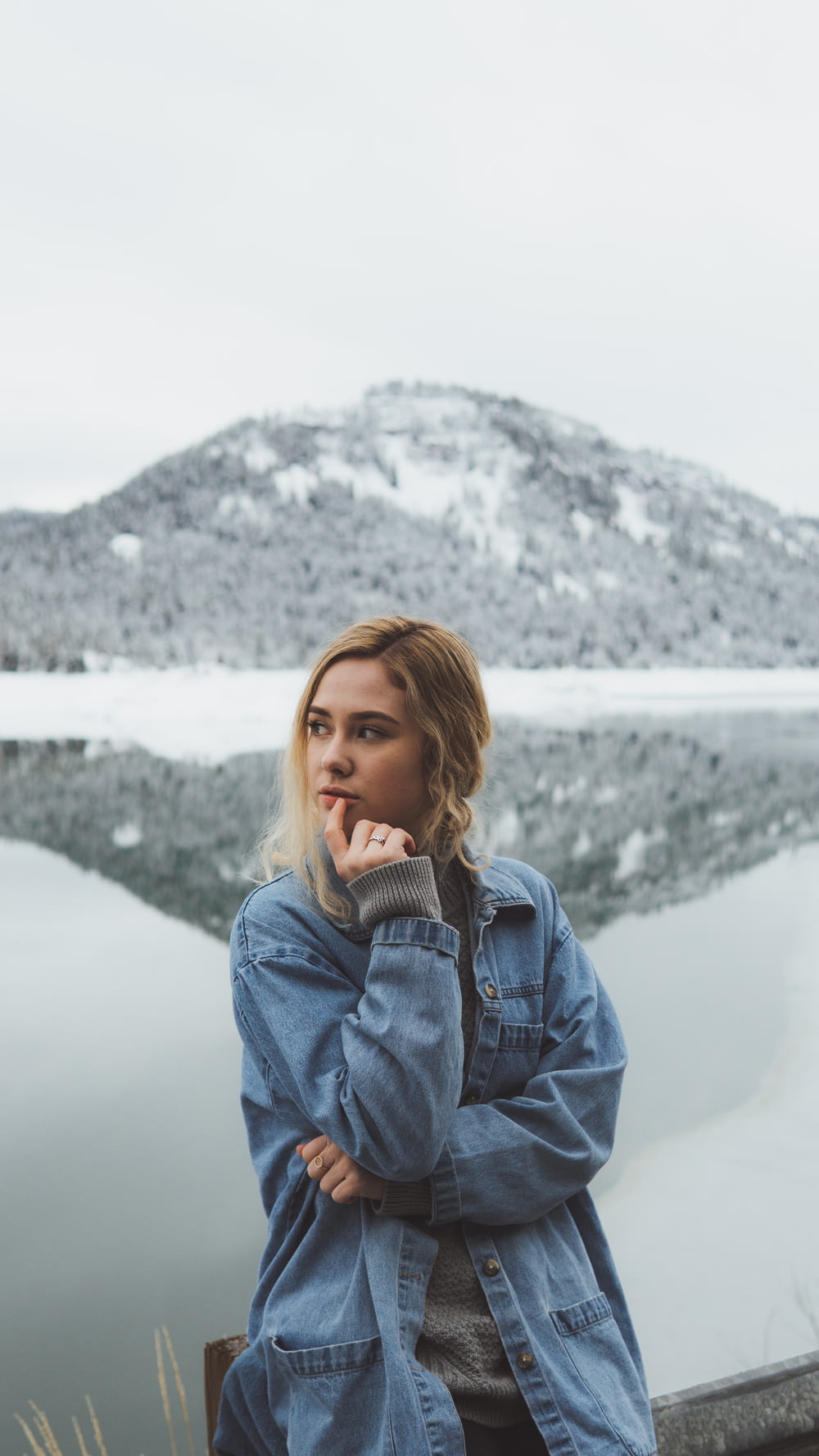 shallow focus photo of woman in blue denim jacket standing near mountain