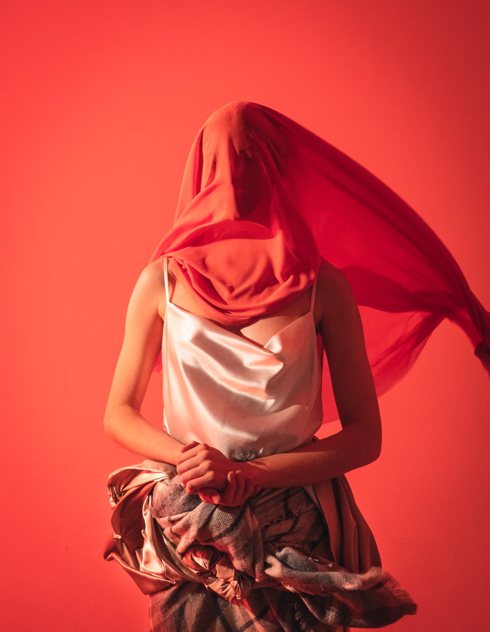 woman with white silk tank top covering face with red cloth
