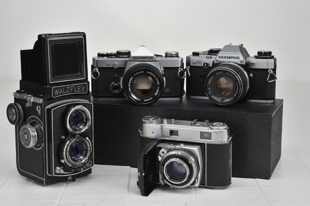 Quattro fotocamere grigie vintage su superficie bianca