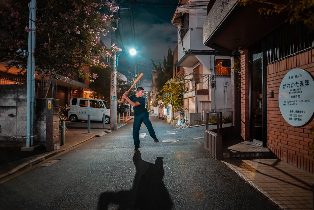 man in black shirt holding baseball bat at street during nighttime