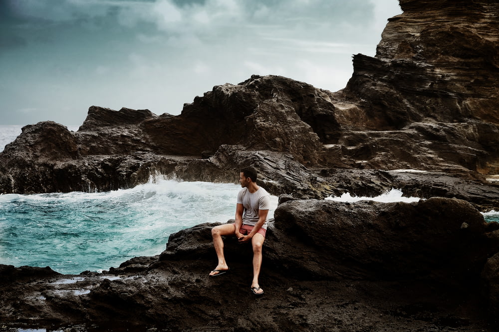 man in shirt sitting on rock formation
