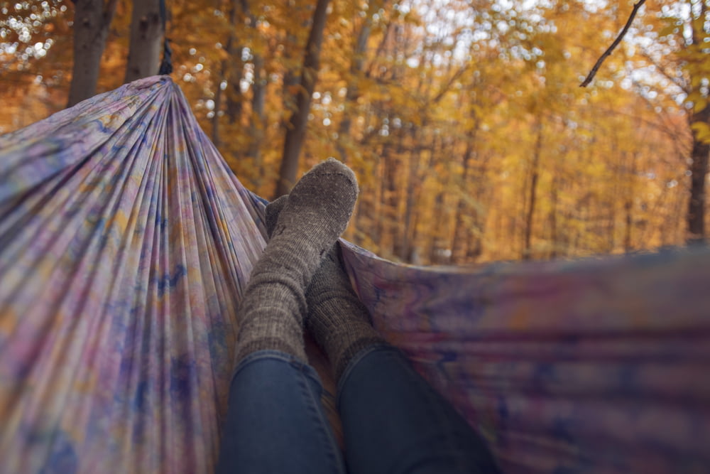pessoa deitada usando meias cinzas deitada em rede multicolorida