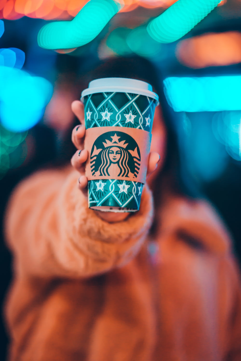 Frau auf brauner Jacke zeigt grüne und braune Starbucks-Kaffeetasse