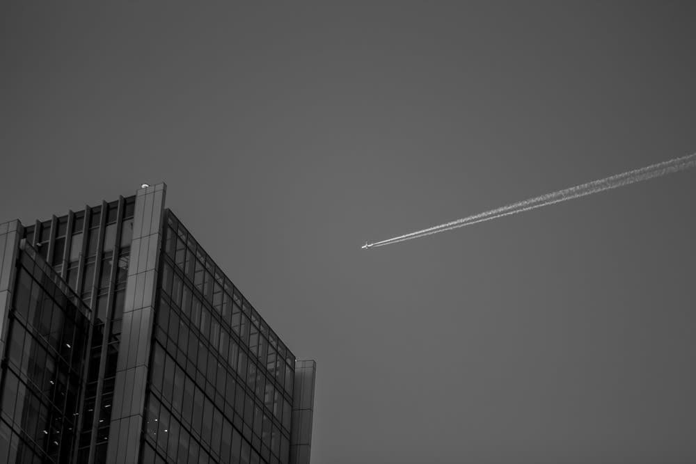 plane above curtain wall building in grayscale photography