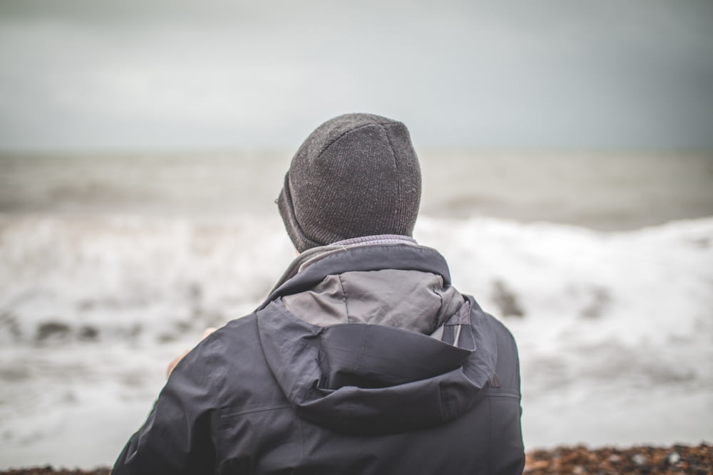 man wearing blue-and-gray hoodie and knit cap near ocean during daytime