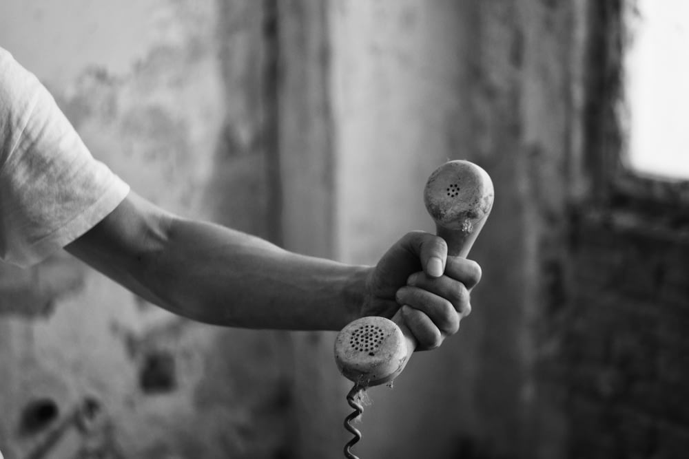 person holding telephone in grayscale phot