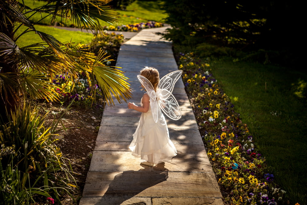 fille portant un costume d’ange debout sur un chemin en bois