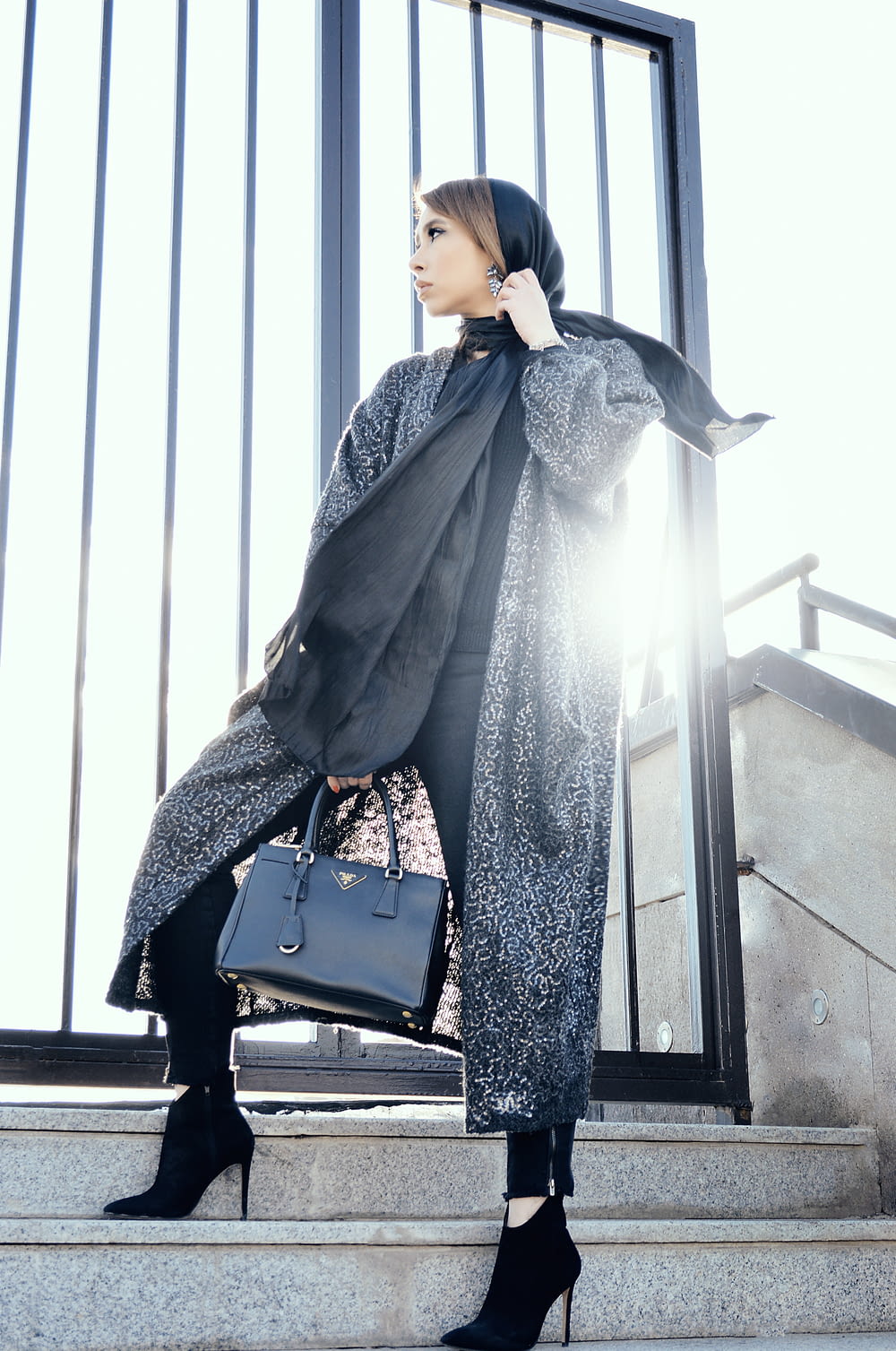 woman in gray coat holding black handbag standing on gray stairs during daytime