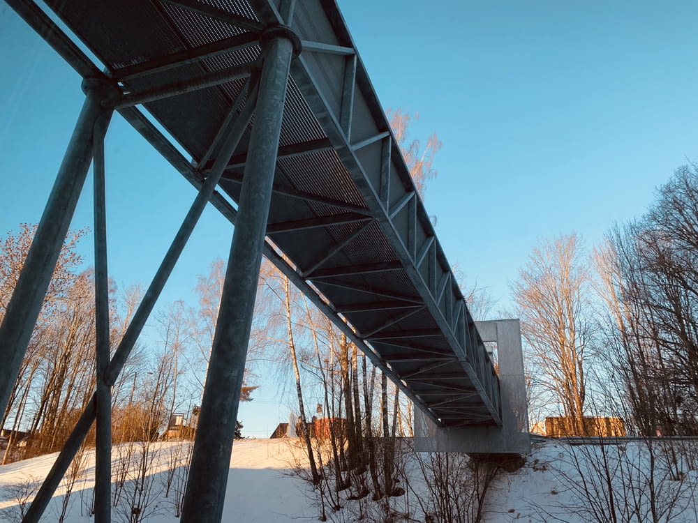 gray metal bridge above snow under blue sky