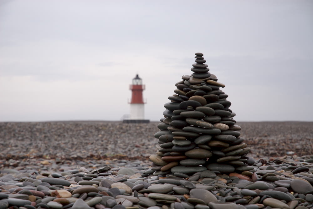 selective focus photography of stocked stones with lighthouse background
