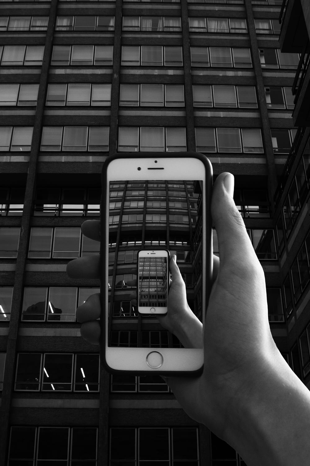 grayscale photography of person holding iPhone taking photo of building