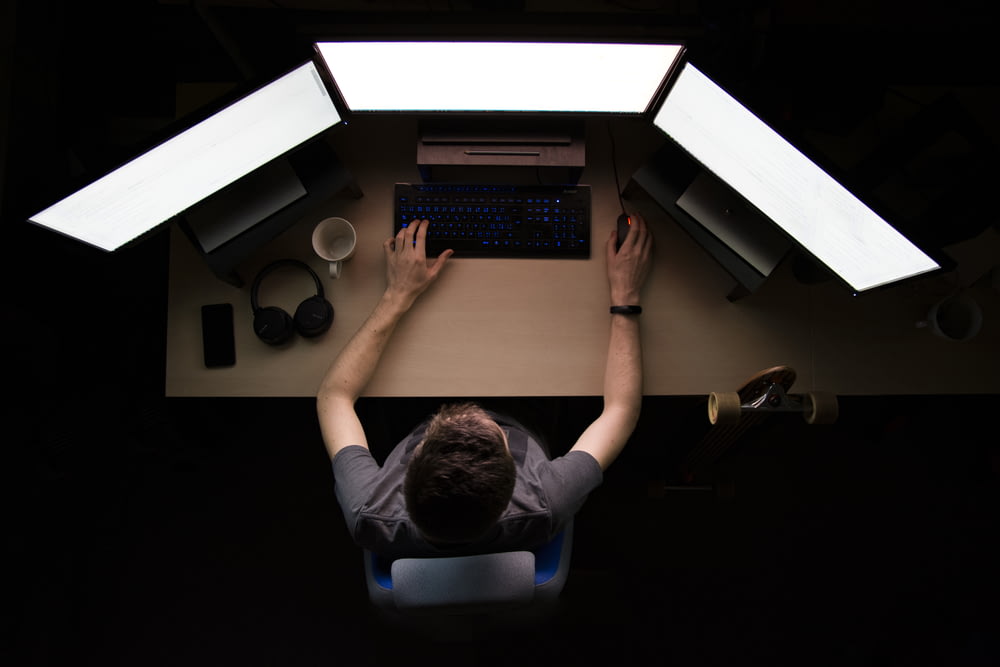 uomo di fronte a tre monitor di computer mentre è seduto