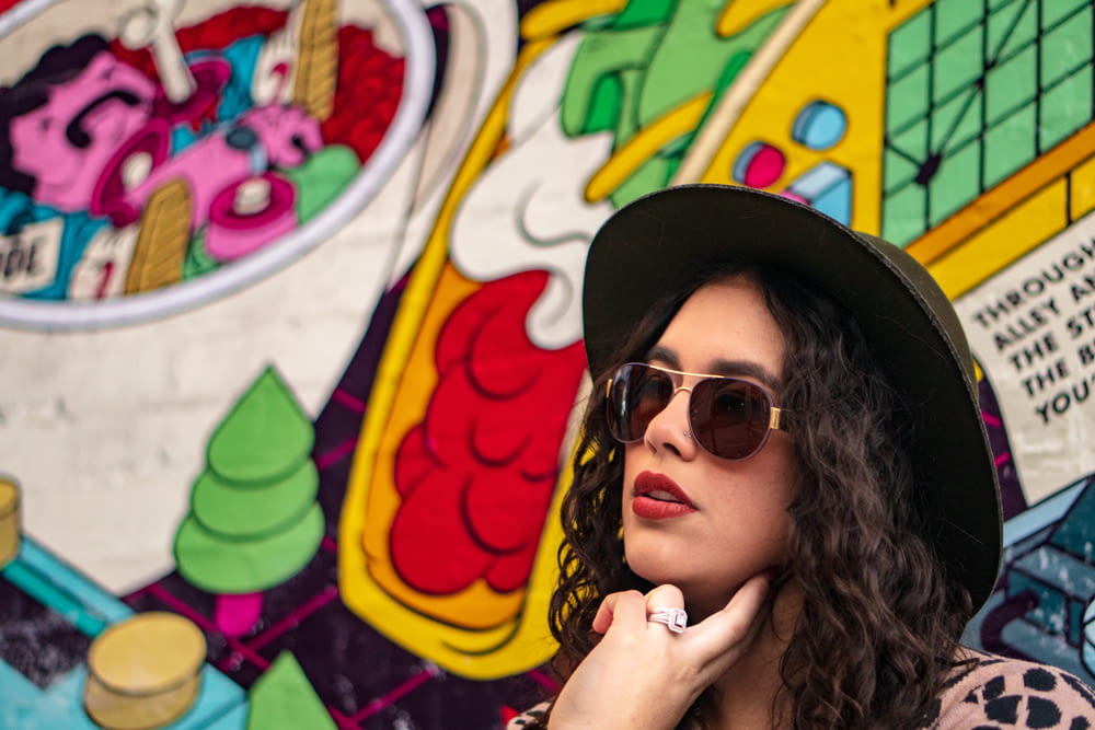 woman wearing black sunglasses and hat beside graffiti