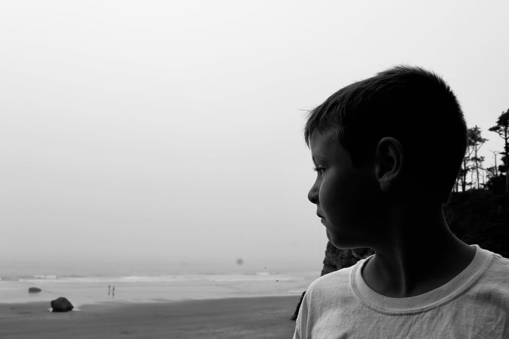 grayscale photography of boy near seashore