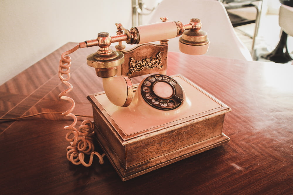 Teléfono giratorio blanco y marrón sobre mesa de madera marrón