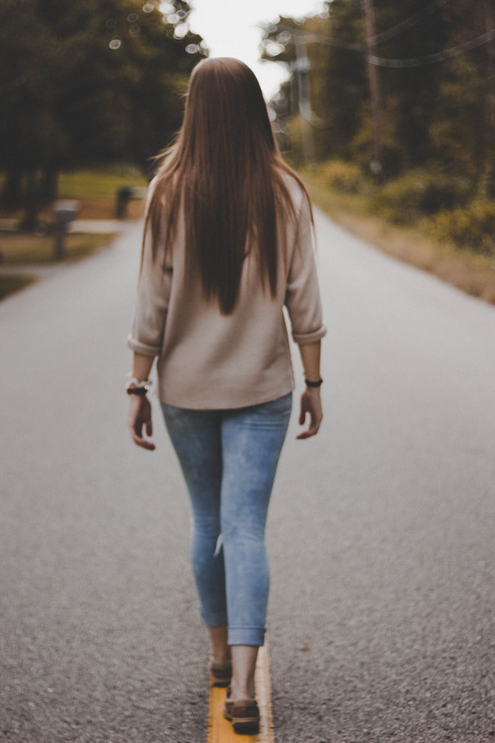 woman in grey shirt and blue denim pants walking on road during daytime