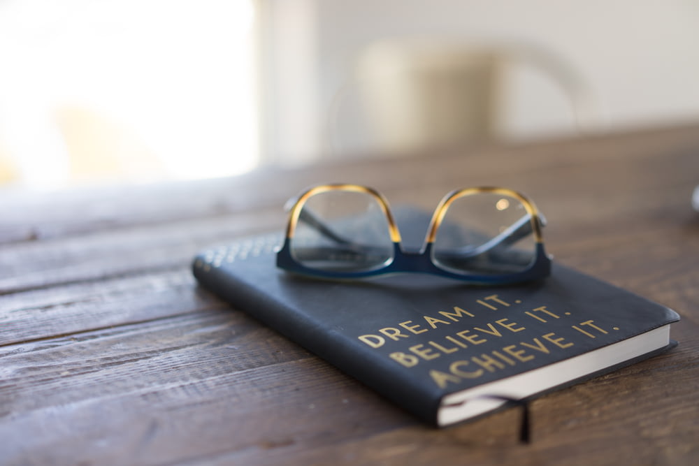 茶色の木製のテーブルの上の本に黒と茶色の眼鏡