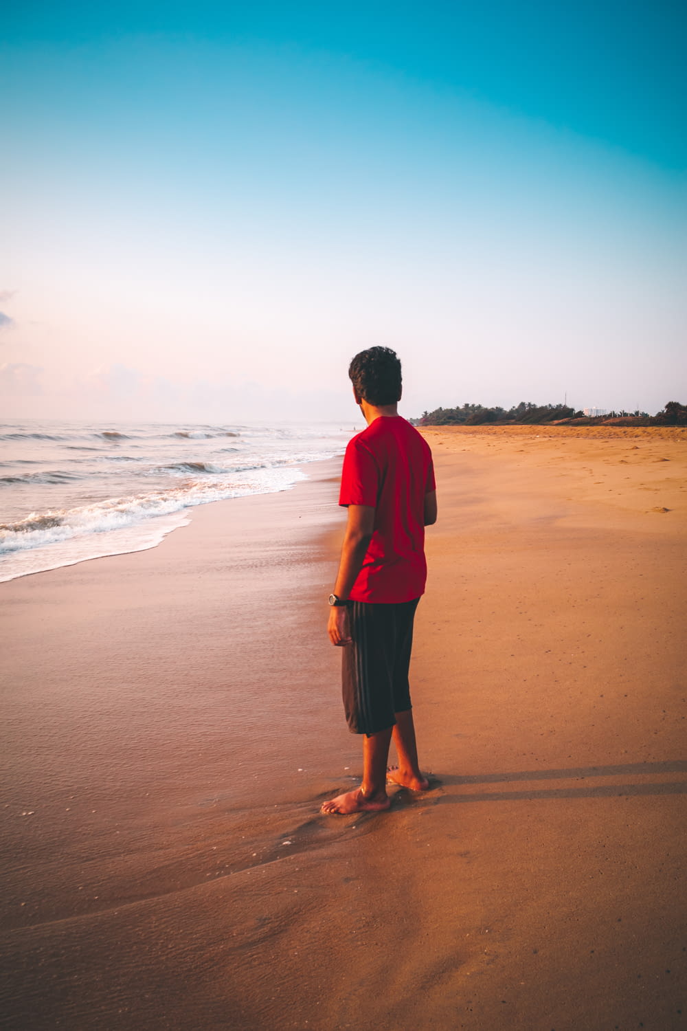 man wearing red shirt standing on the seashore