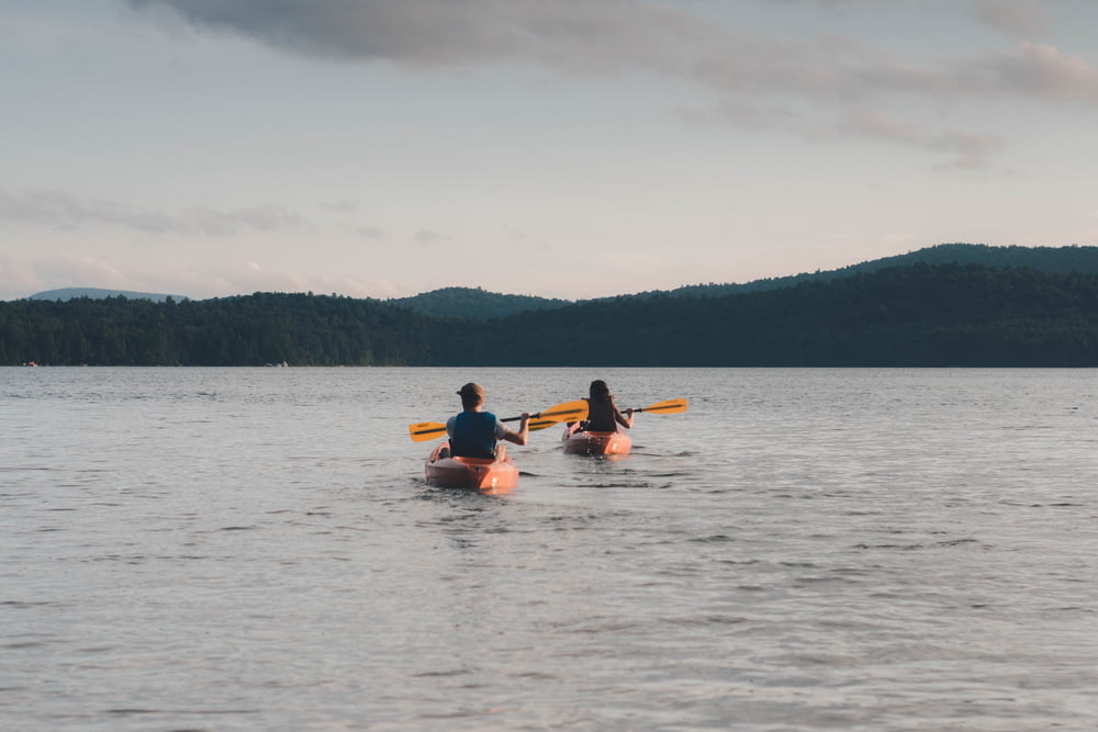 man and woman riding kayaks paddling on calm body of water