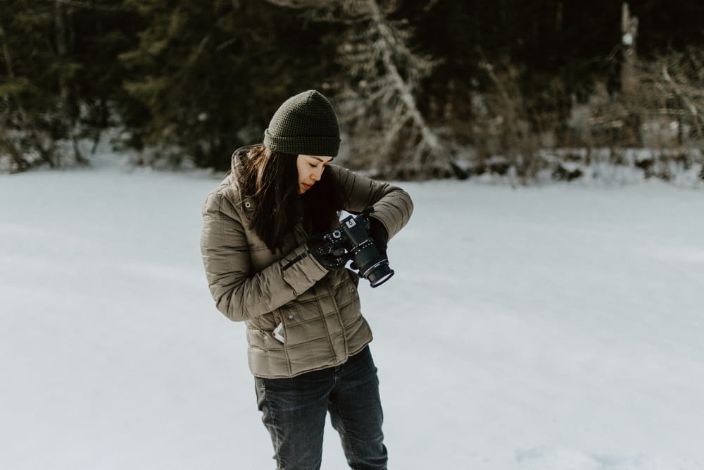 woman holding black digital camera standing on ground filled with snow